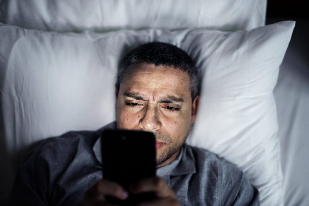 Uomo che usa lo smartphone nel letto